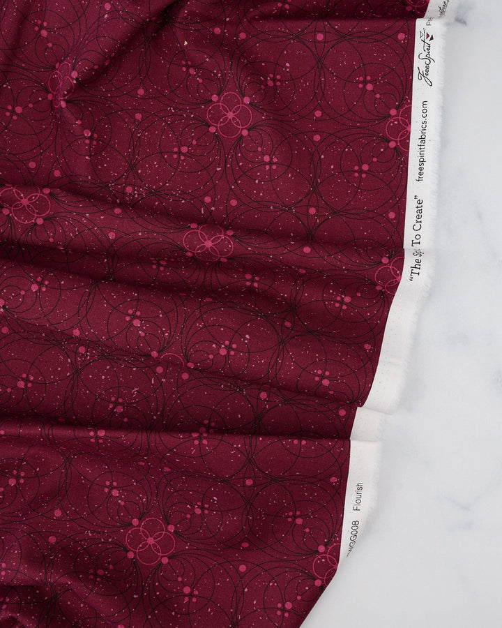 A swatch of 'Flourish in Garnet' fabric from the 'Enrapture' collection by Giucy Giuce for Free Spirit Fabrics, displaying a floral pattern on a garnet red background.