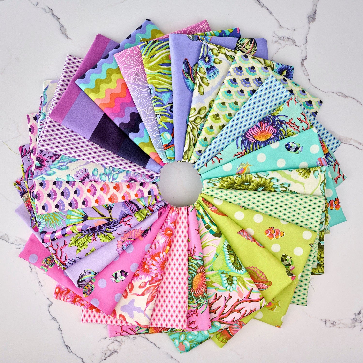 Collection of colorful Floral Reef fabric swatches arranged in a circular pattern on a marble surface, designed by Tula Pink