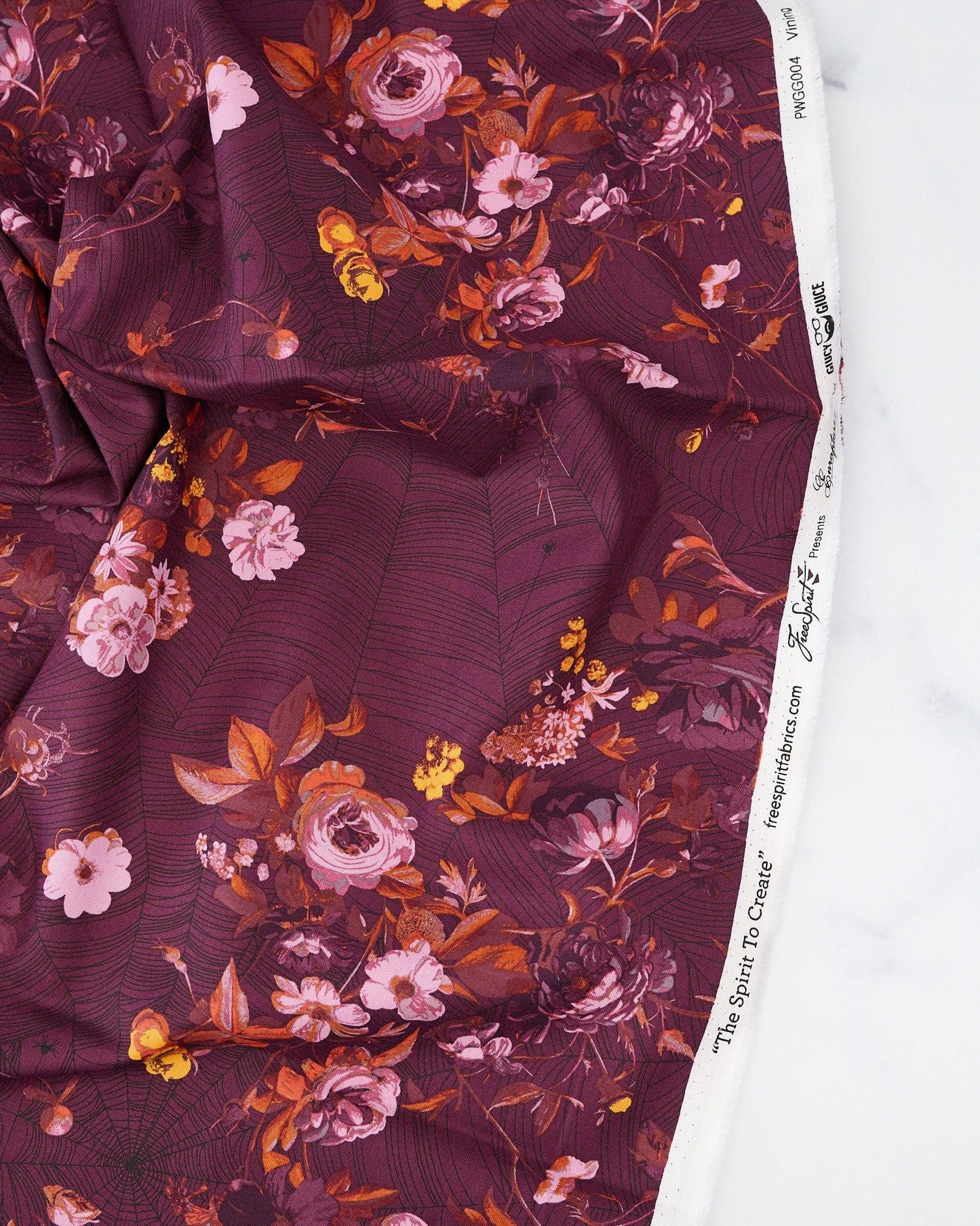 A piece of fabric featuring a floral pattern with shades of purple, pink, and orange on a red background.
