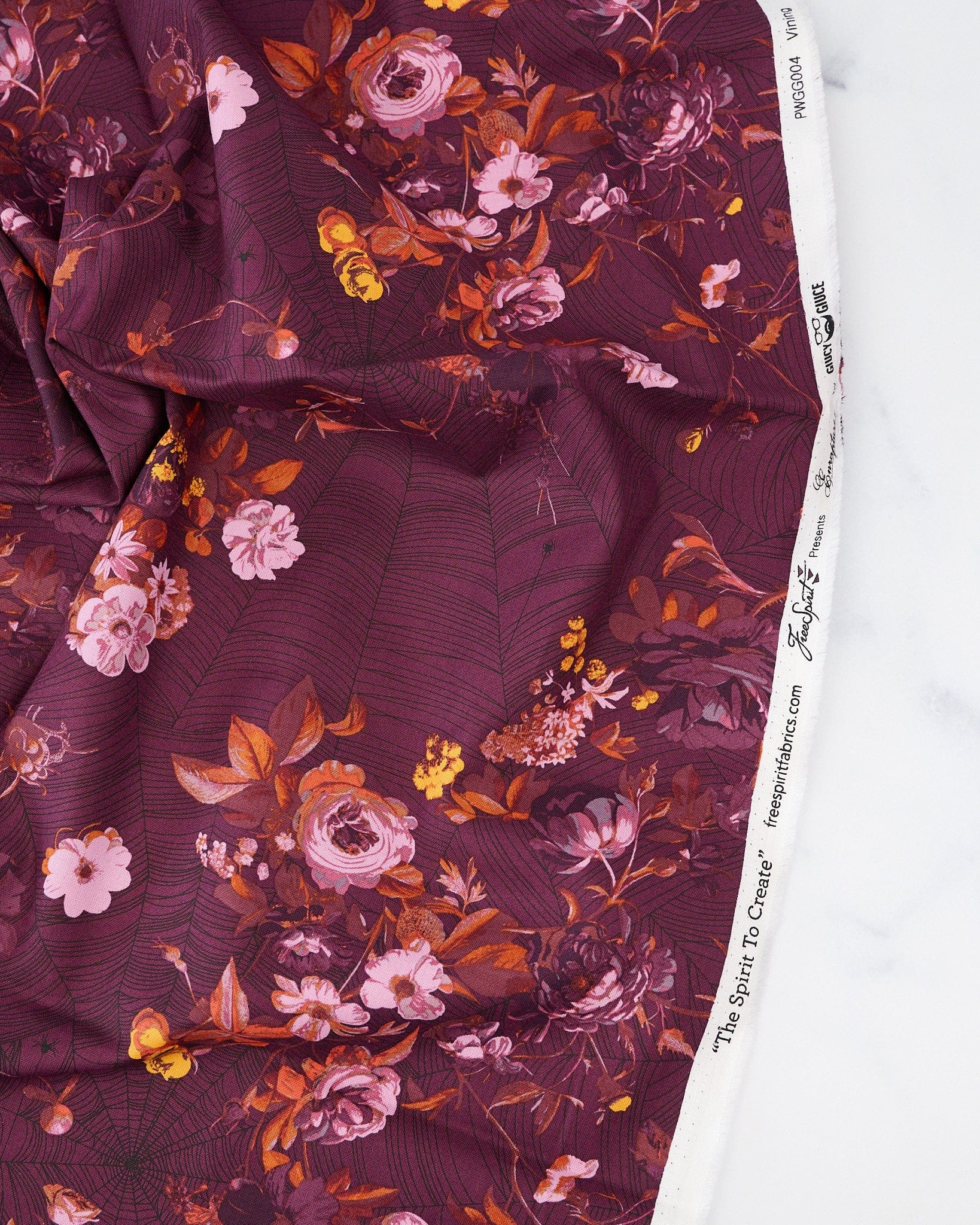 A piece of fabric featuring a floral pattern with shades of purple, pink, and orange on a red background.
