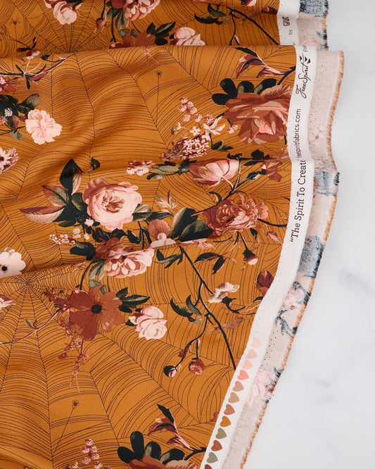 A piece of burnt orange/gold spice colored fabric with a floral pattern designed by Giucy Giuce for Free Spirit Fabrics, part of the Enrapture collection.
