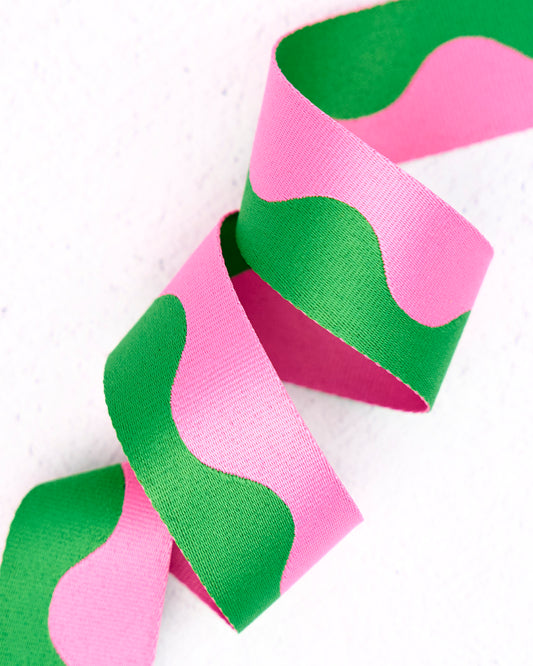 Close-up of wavy nylon webbing by Renaissance Ribbons, featuring a flowing pattern in soft bubblegum pink and vibrant grassy green, curled into gentle loops against a clean white background.